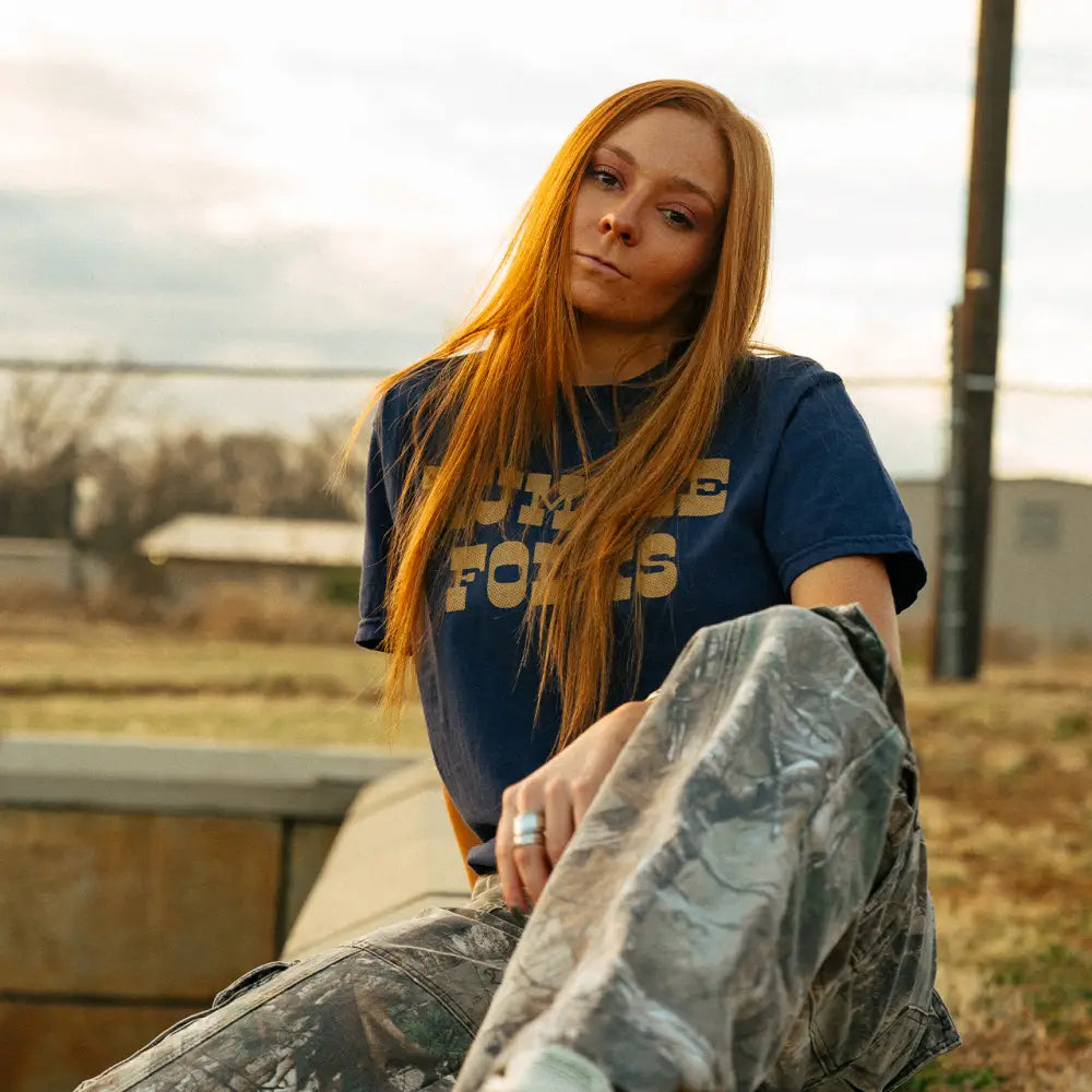 Young woman with long red hair wearing a blue Air Force t-shirt and camouflage pants.