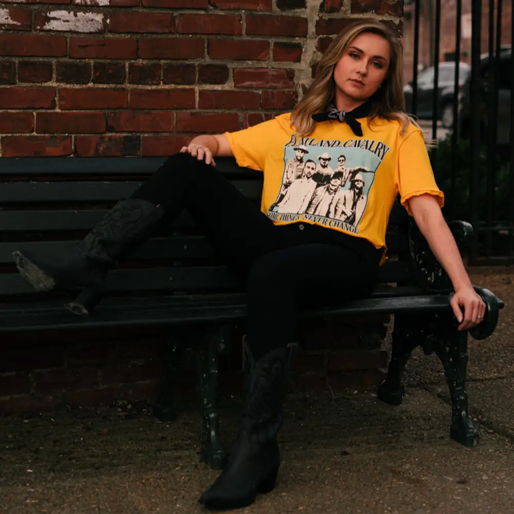 Woman wearing a yellow t-shirt with a graphic print, sitting on a bench.