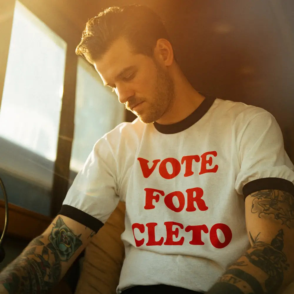 Man wearing a white t-shirt with red text saying ’VOTE FOR CLETO’.