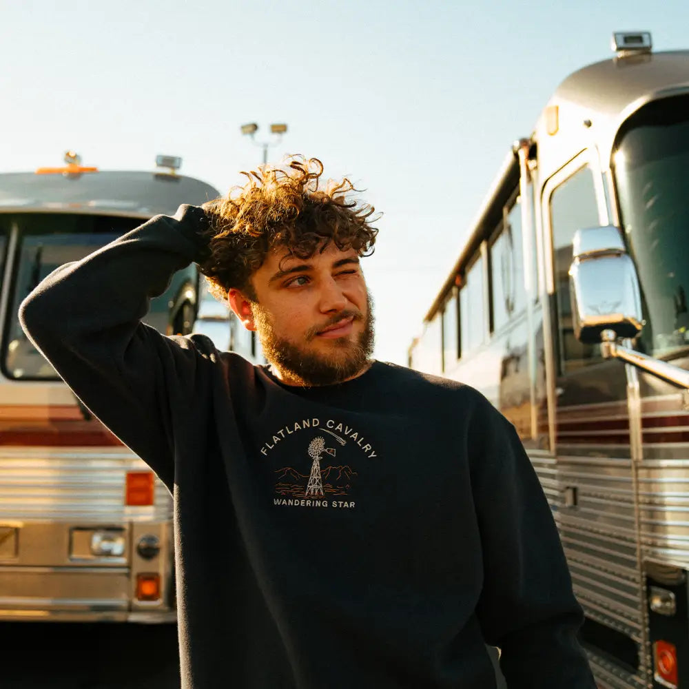 Young man with curly hair wearing a dark sweatshirt standing in front of buses.